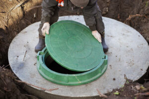 A worker installs a sewer manhole on a septic tank made of concrete rings. Construction of sewerage networks for country houses.