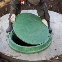 A worker installs a sewer manhole on a septic tank made of concrete rings. Construction of sewerage networks for country houses.